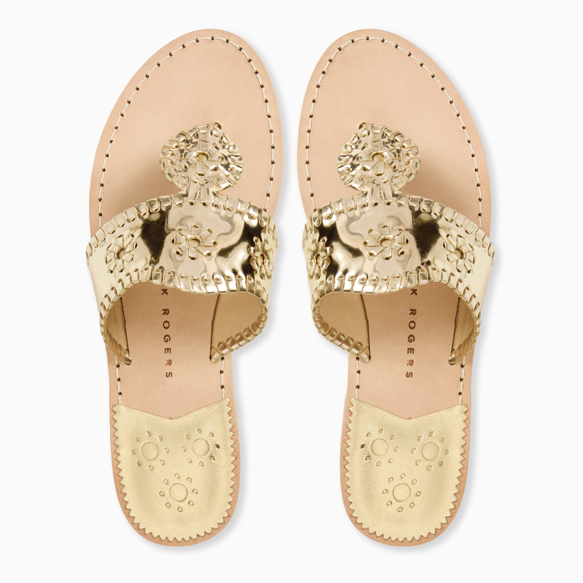 A pair of gold metallic slide sandals with ornate whipstitch rondel medallion details on the strap, shown from a top-down view on a white background. 